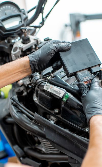 Electrician or repairman in protective gloves connecting wiring in the motorcycle during a repairment at the workshop, close-up