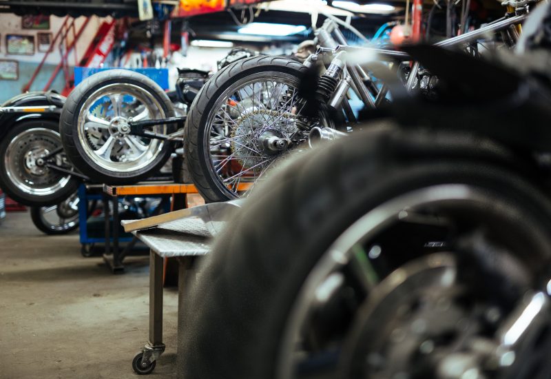 Background image of several motorcycles on stands in repair shop with back wheels in row