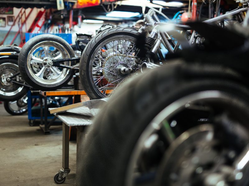 Background image of several motorcycles on stands in repair shop with back wheels in row